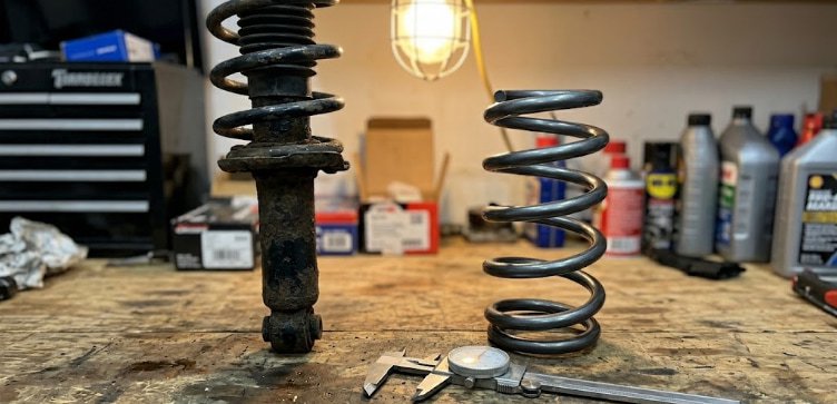 Stock damper and aftermarket lowering spring comparison worn factory shock absorber with chipped paint next to a new lowering spring on a workbench